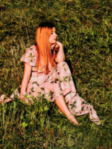 Photo of the singer - a woman in a flowered dress sitting on the grass
