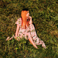 Photo of the singer - a woman in a flowered dress sitting on the grass