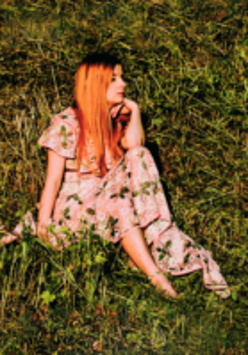 Photo of the singer - a woman in a flowered dress sitting on the grass