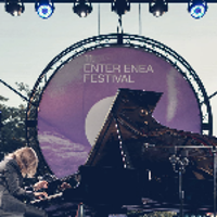 Photo of Leszek Możdżer playing the piano on an open-air stage.