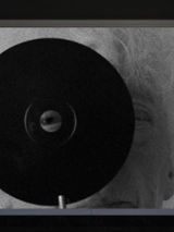 Black and white picture of an elderly woman with gray hair, looking through the hole in a black circle
