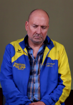 Exhibition poster: photo of a sad looking man in blue and yellow shirt and jacket.