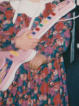 One of the exhibition works: a child, with its face unvisible, holding a toy guitar.