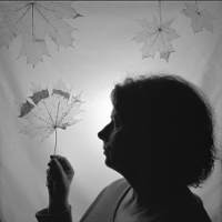 Black and white picture of a middle-aged woman in profile, holding a leaf in her hand. Three other leaves in the top of the photo