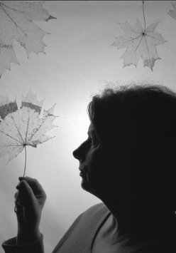 Black and white picture of a middle-aged woman in profile, holding a leaf in her hand. Three other leaves in the top of the photo