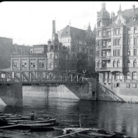 Black and white photo of buildings from past centuries by the river and a bridge.