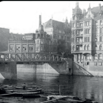 Black and white photo of buildings from past centuries by the river and a bridge.