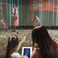 Two girls, standing back to the camera, in front of a mockup made of Lego bricks.