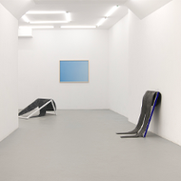 Picture of the white room with one blue picture on the wall and two exhibits by the walls.