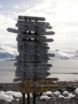 One of the exhibition works: a photo of a pole with many signposts with names of places and distances to them. In the background water and snowy mountains.