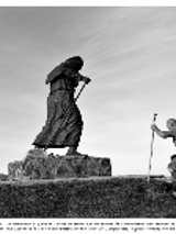 Black and white photo of a monument of a wanderer and a man-wanderer with a backpack and a stick on which he leans.