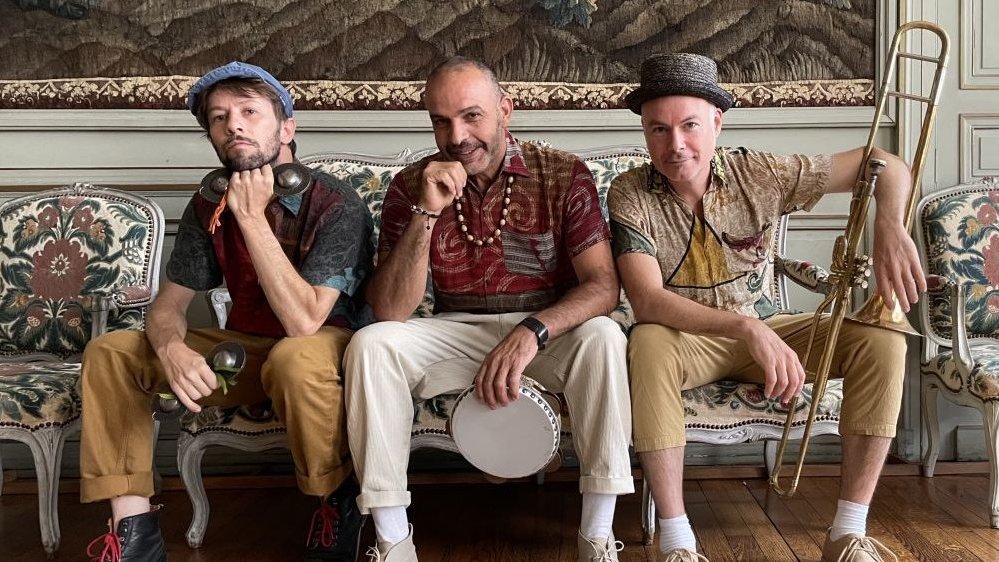 Photo of the band - three men holding their musical instrument, sitting on a sofa.