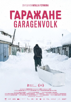 A man pulling a white container-sled in the snow. Low buildings covered with snow around.