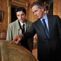 Photo from the movie: two men standing at the globe, one of them is showing something on the globe.