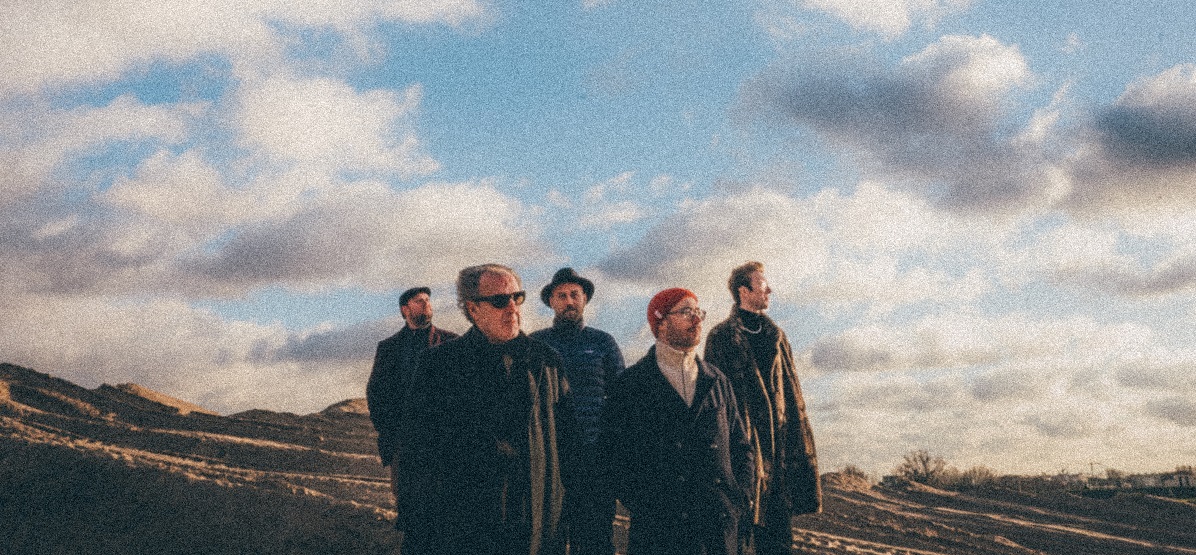 Niechęć, photograph: Mateusz Czech Five men standing on the field, blue sky and white clouds as a background.