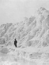 The black-and-white photograph shows a man standing in front of a great snowdrift.