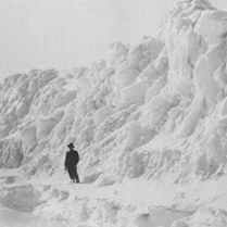 The black-and-white photograph shows a man standing in front of a great snowdrift.