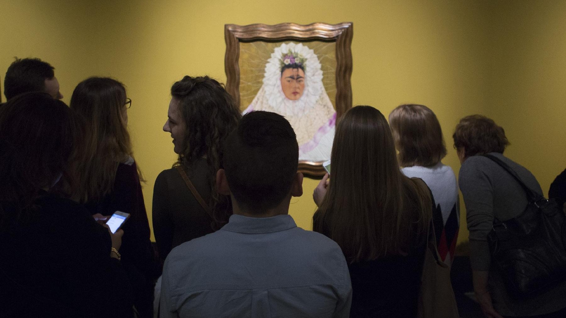 Photo from the exhibition: a few people watching Frida Kahlo's portrait