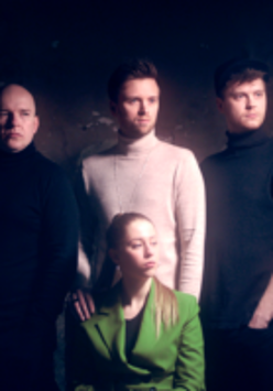 Photo of the band members - three men who are standing behind a woman who is sitting