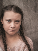 Picture of a girl in braids who is looking into the camera. Grey background.