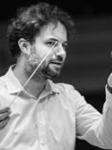 Black and white photo of the conductor Łukasz Borowicz, who is holding a baton in his right hand