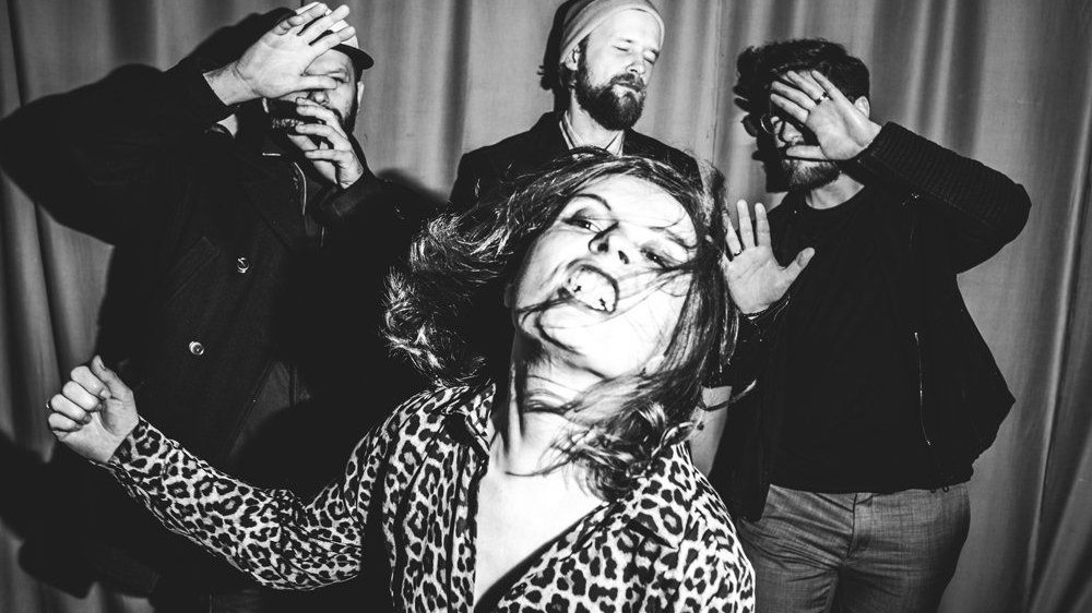 Photo of one woman baring her teeth and three men, two of them are covering their faces with their hands because of dazzling light.