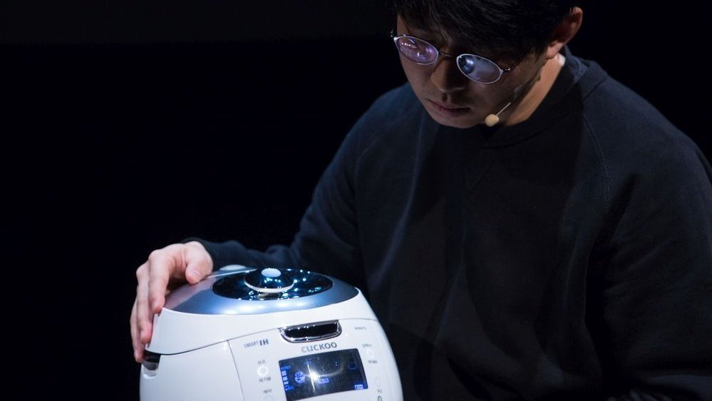 A scene from the performance - a man touching a small robot.