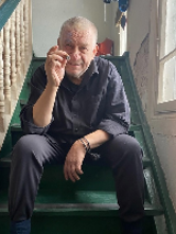 Photo of the artist - a man sitting on stairs wit a cigarette in his hand.