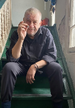 Photo of the artist - a man sitting on stairs wit a cigarette in his hand.