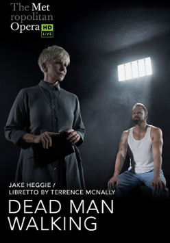 On the left there is a woman with short white hair and in a long gray dress, facing right. On the right sits a muscular man in a white T-shirt and light jeans. He looks at the woman. The setting is a prison cell.