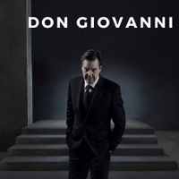 Photo of a man in black suit with hands in pockets in a dark room.