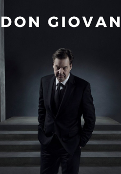 Photo of a man in black suit with hands in pockets in a dark room.