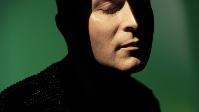 Photo of Michał Pepol, with his face illuminated; green background.