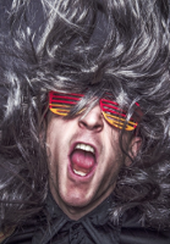 Photo of a man's face with open mouth, colourful glasses and curly hair.