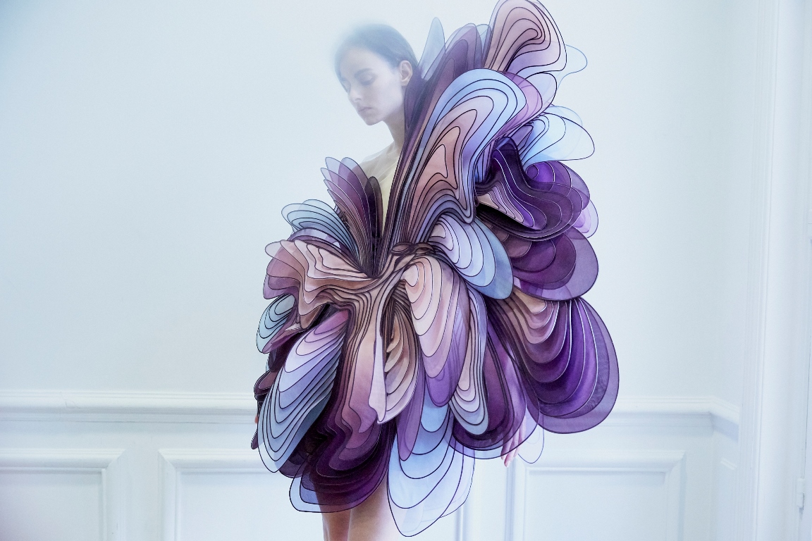 A photo of a woman dressed in blue, purple and pink cloth which looks like many butterfly's wings. White background - grafika artykułu