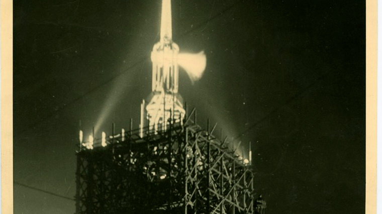 Night-time lighting of the town hall tower reconstructed from war-time damage on the day a historic eagle emblem was raised to its top in 1947. On the left - damaged tenement houses.