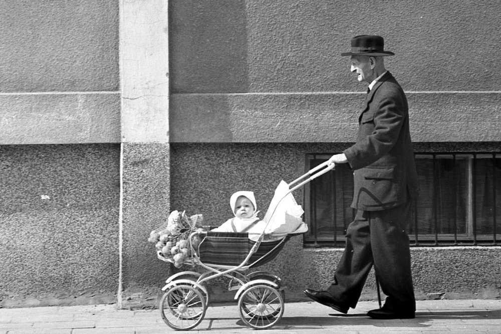 Black and white photo of an eldery man pushing a pram with a baby - grafika artykułu