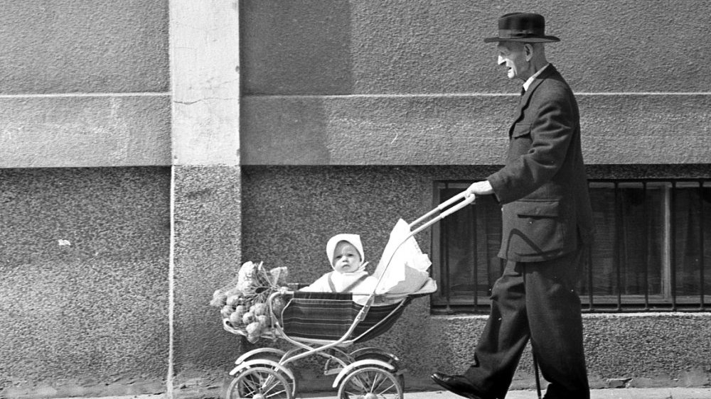 Black and white photo of an eldery man pushing a pram with a baby