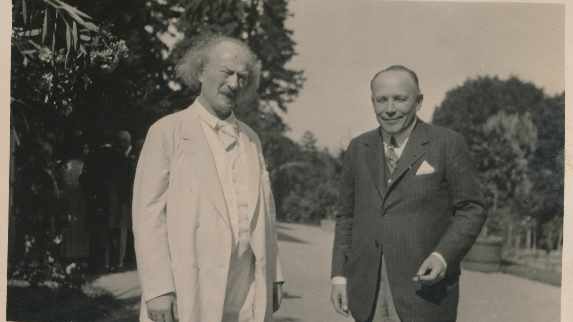 Black and white picture of two elegantly dressed men (one of them Ignacy Jan Paderewski) standing on the road, trees in the background.
