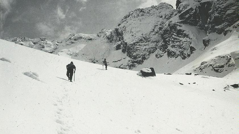 Black and white photo of snow-covered mountains.Two men going through the snow.