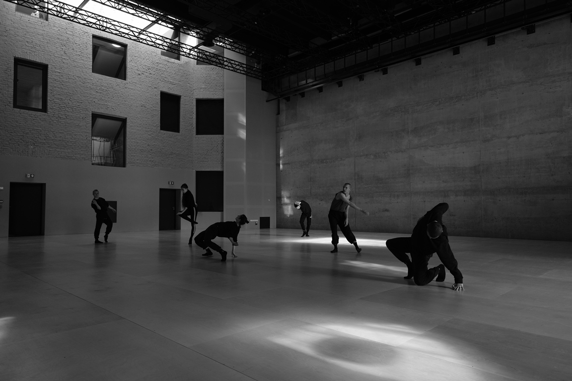 Black and white photo of dancers in various poses in empty, modern space. - grafika artykułu