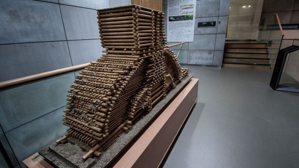 Wooden construction made of numerous wooden stakes on a concrete wall background. Stairs on the right.
