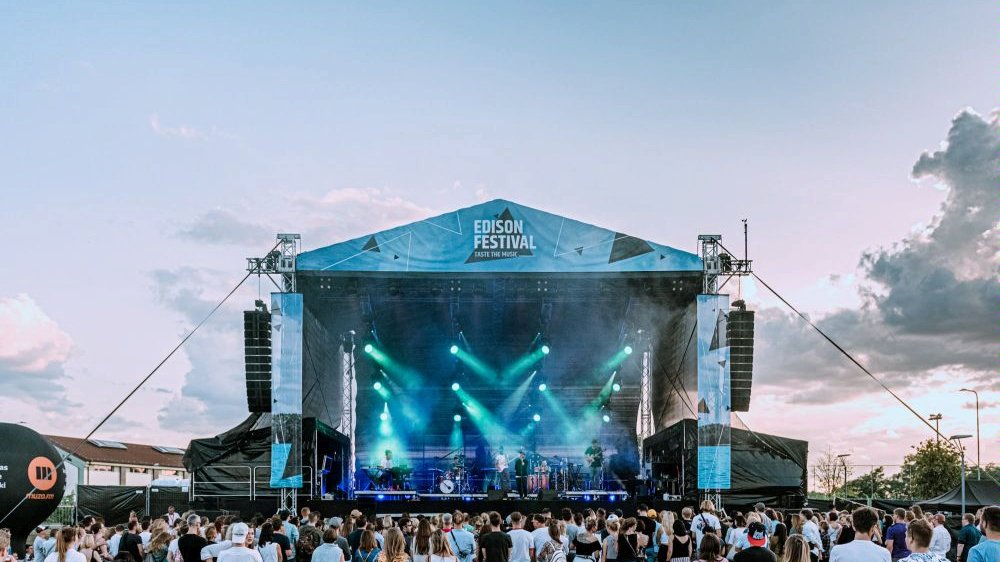 The photo shows the outdoor stage and the people standing in front of the stage. There is a band performing on the stage. - grafika artykułu