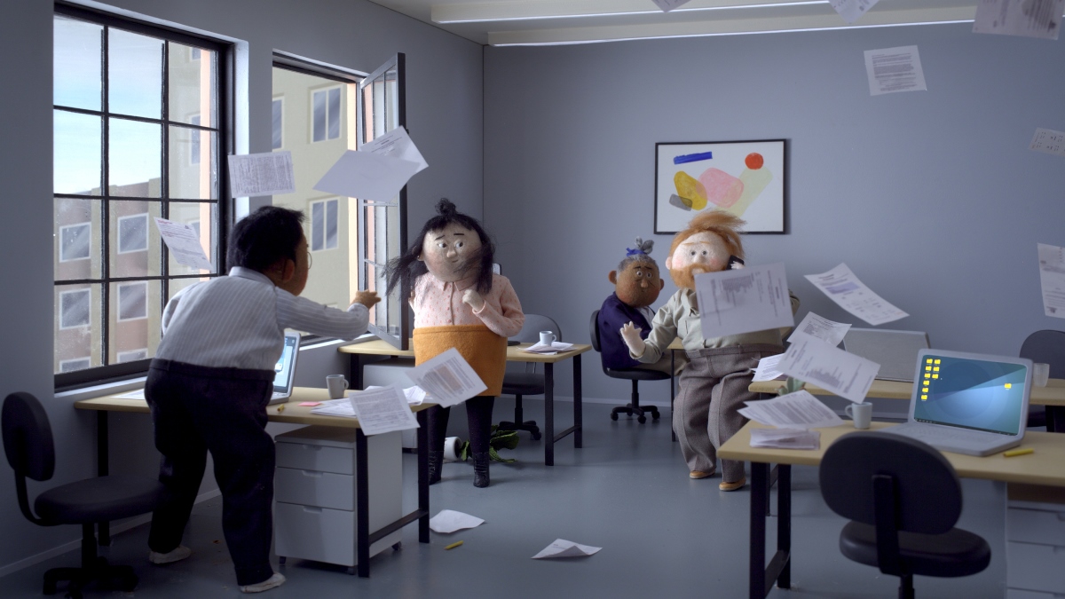 Picture from animated film: the room with open window, with 4 people in, who stand or sit by their desks. Because of wind some sheets of paper are floating in the air. - grafika artykułu