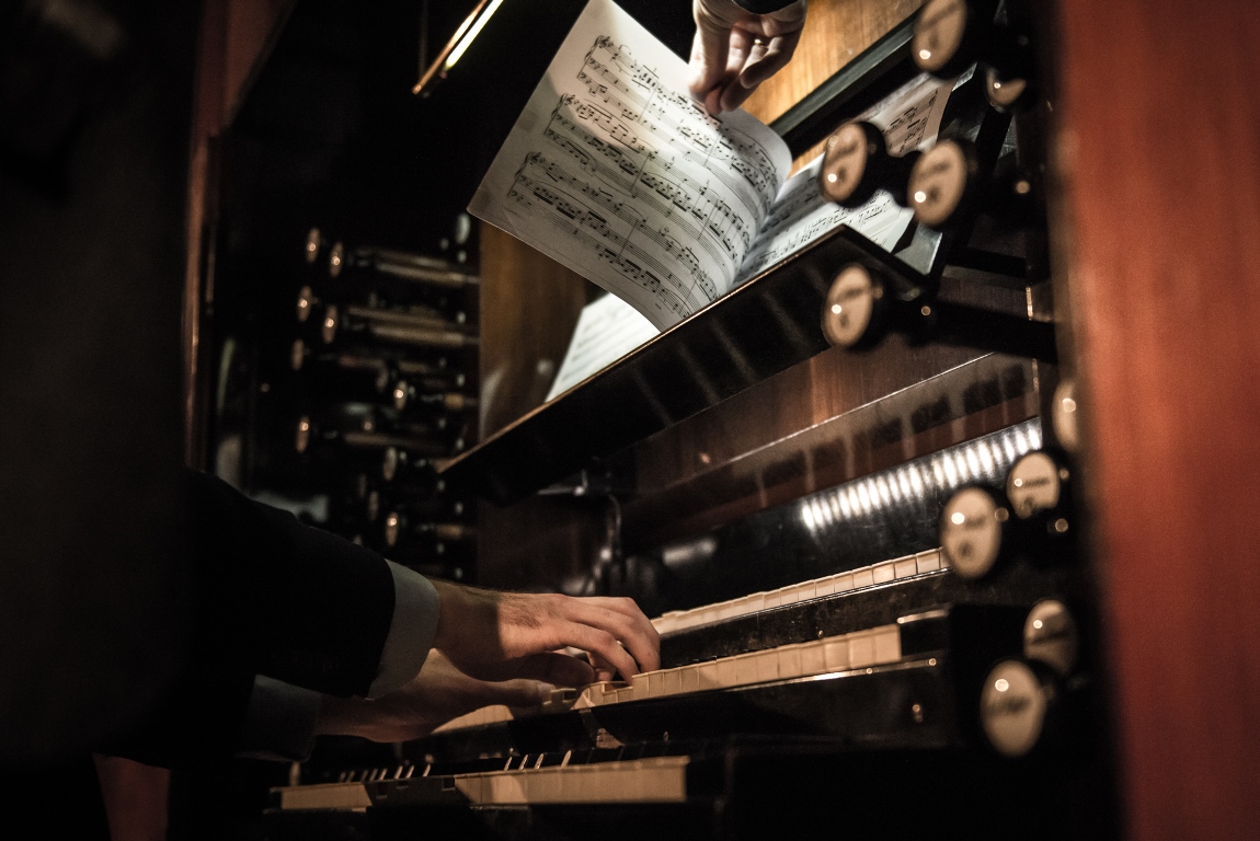 A part of pipe organ. The photo shows a musician's hands on a keyboard and pages with notes - grafika artykułu