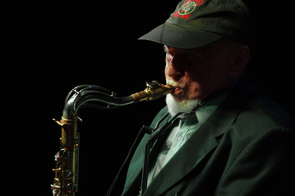 Photo of Jan "Ptaszyn" Wróblewski - a man playing the saxophone on a black background - grafika artykułu