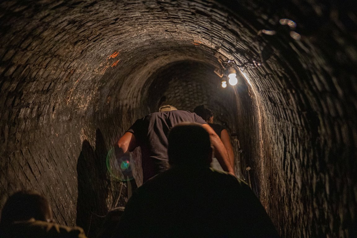 Underground corridor lit by two light bulbs and 3 people walking down the corridor - grafika artykułu