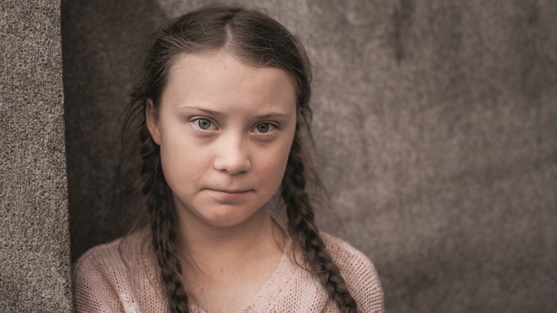Picture of a girl in braids who is looking into the camera. Grey background. - grafika artykułu