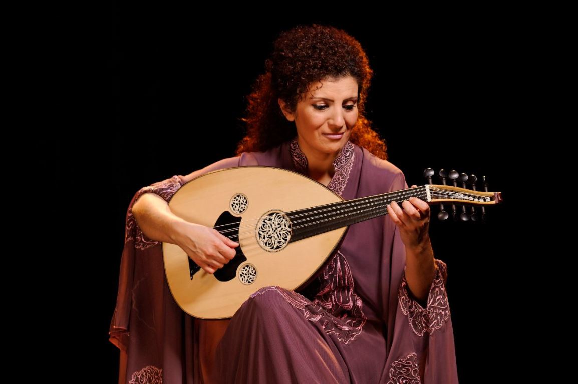 Photo of a woman in a long dress. The artist sits and holds an oval stringed instrument in her hands - grafika artykułu