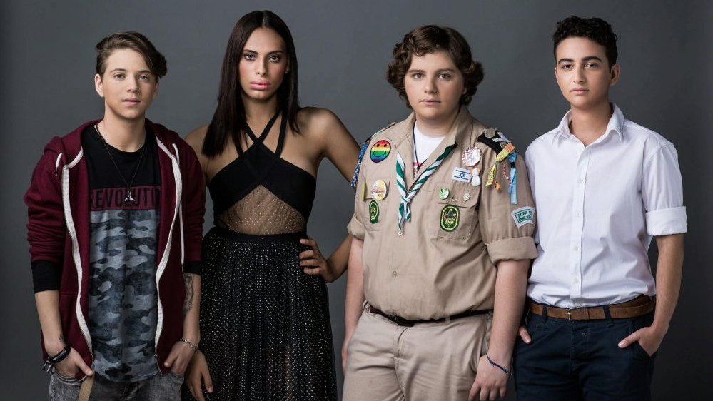 Photo from the movie: four young people who are standing and looking into the camera. Grey wall as a background.